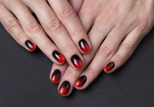 Two female hands with red black ombre gradient nails on dark background — Stock Photo, Image