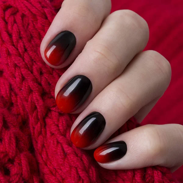 Main féminine avec des ongles gradient ombre rouge noir tenir tissu textile de laine — Photo