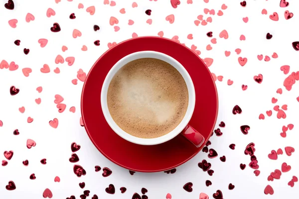 Red sparkles confetti in heart shape and cup of coffee on white — Stock Photo, Image
