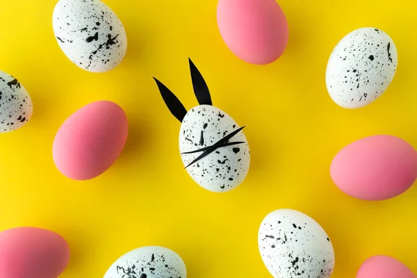 Composición de Pascua con huevos de colores y huevo con orejas de conejo y cara sobre fondo amarillo — Foto de Stock