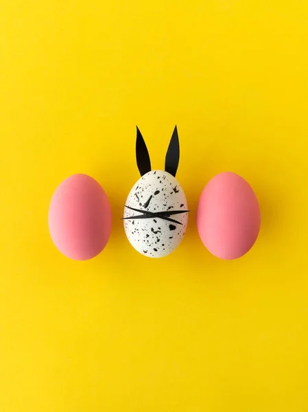 Composición de Pascua con huevos de colores y huevo con orejas de conejo y cara sobre fondo amarillo — Foto de Stock