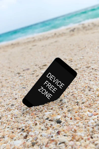 Spartphone with text device free zone written in its screen placed in the sand of a beach. Social media gadget internet addiction concept