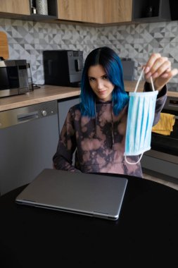 Mavi saçlı, koruyucu maske takan genç bir kadın. Virüs dünya paniği salgını. Karantina konseptinin sonunda evde kal.