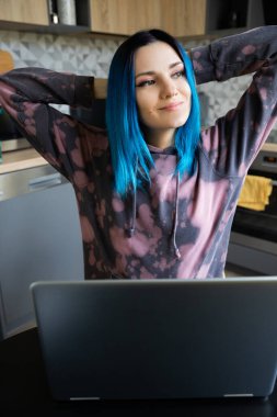 Mavi saçlı, mutlu, genç hippi kadın. Mutfakta dizüstü bilgisayarı var. Başarılı gülümseyen kadın ev konseptinden çalışıyor..