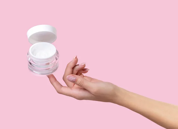 Pot ouvert avec crème cosmétique à la main de femme sur fond rose . — Photo