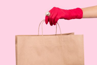 Kadınlar pembe arka planda kağıt torba tutan kauçuk bir eldiven veriyorlar. Güvenli ev teslimatı konsepti.