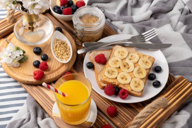 Yatakta kahvaltı. Tahta tepside bir bardak portakal suyu ve böğürtlenli sandviç. Sabah sağlıklı ev yapımı kahvaltı.