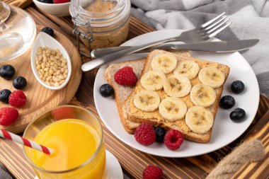 Yatakta kahvaltı. Tahta tepside bir bardak portakal suyu ve böğürtlenli sandviç. Sabah sağlıklı ev yapımı kahvaltı.