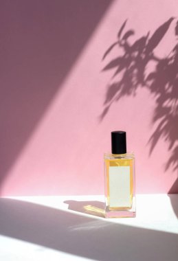 Pembe arka planda, güneş ışığı gölgeli bir şişe esans parfümü. Asgari biçim parfüm şablonu