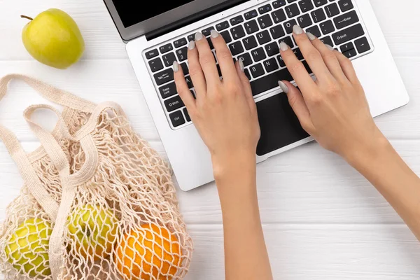 İnternetten yiyecek alışverişi. Ahşap masada meyve ve dizüstü bilgisayarlı çevre dostu doğal çanta. Sıfır atık.