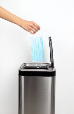 Kadın eli gri arka plandaki çöp kutusuna koruyucu bir maske atıyor. Karantina kavramının sonu