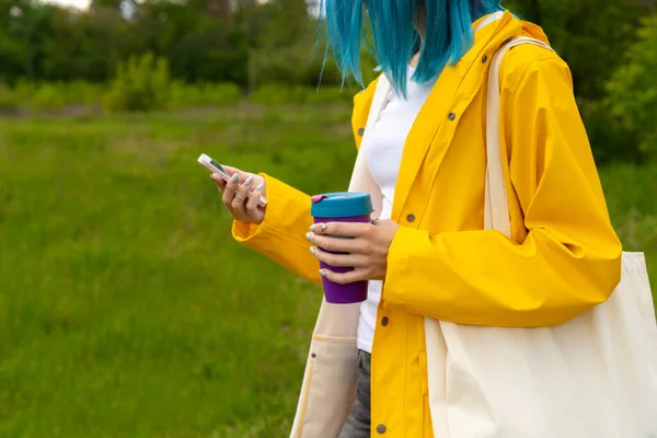 Açık hava bahçesinde elinde sıcak içecekle duran mavi saçlı genç ve güzel bir kadın. Sürdürülebilir yaşam tarzı. Çevre dostu kavram.