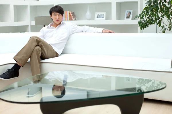 young asian man lying on sofa and looking at camera
