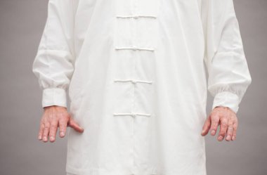 Beyaz gömlekli ve siyah eldivenli bir adam gri arka planda el ele tutuşuyor.