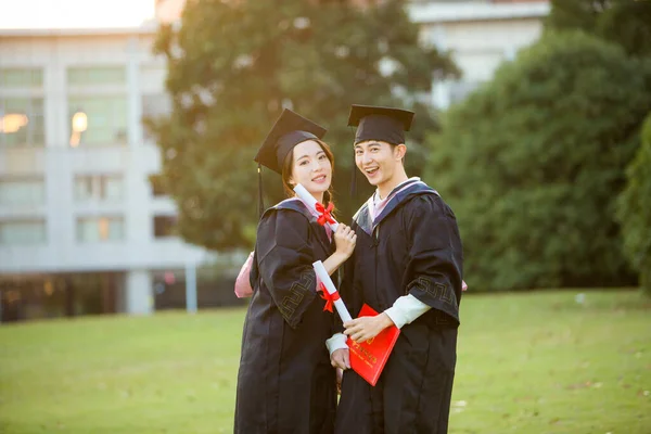 happy young couple in graduation hats and gown with diploma in the background
