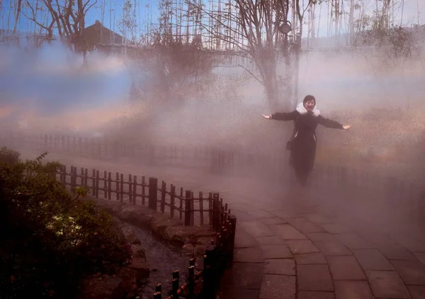 a man in a black suit is walking in the fog.