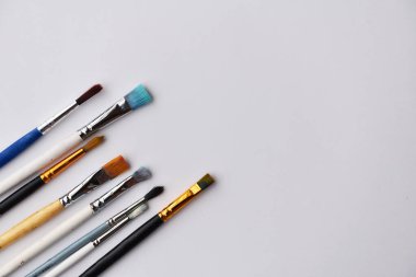 Boyalarla resim yapmak için fırçalar. Beyaz arka planda, metin için bir yer var. Fırçanın ahşap tabanı ve sentetik yığını var. Farklı boyutlarda fırçalar, farklı tipler, farklı renkler, kullanılmış