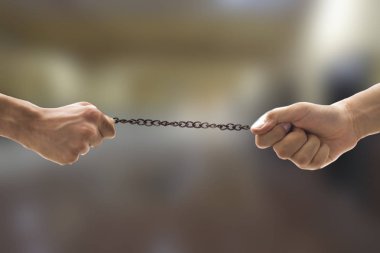 Ofis otoparkındaki kurumsal sektörün bulanık arka planına sahip paslı metal bir zincirle çekişirken yakın plan çekilen iki el..
