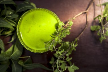 Tulsi, fesleğen, neem ya da Hint leylağı ezmesi ile kahverengi ahşap bir yüzey üzerinde taze neem ve tulsi yapraklarıyla dolu cam kaseyi yakın çekim yapın..