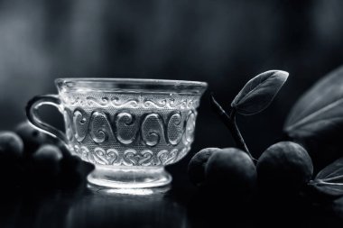 Bitkisel ayurvedik banyan ağacı çayı ya da şeffaf cam fincanda Hint dilek ağacı çayı ile siyah parlak bir zemin üzerinde biraz olgun ve çiğ banyan meyvesi ve bulanık bir arka plan..