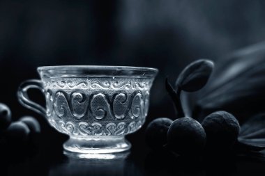Bitkisel ayurvedik banyan ağacı çayı ya da şeffaf cam fincanda Hint dilek ağacı çayı ile siyah parlak bir zemin üzerinde biraz olgun ve çiğ banyan meyvesi ve bulanık bir arka plan..