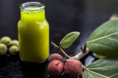 Banyan Ağacı, şeffaf cam bir şişeyle siyah parlak bir yüzey ve olgun ve çiğ banyan ağacının meyveleriyle yakın plan çekilmiş. Yatay çekim.