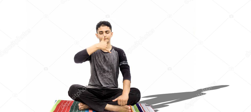 Full body shot of male teenager doing Nadi Shdhana Pranayama or Alternate Nostril Breathing isolated on white background. Male yoga pose. Horizontal shot.