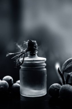 Şeffaf cam bir şişede banyan ağacı yağı ve biraz banyan meyvesi ile birlikte siyah parlak ahşap bir yüzey üzerinde yaprağını yakın çekim. Dikey çekim.