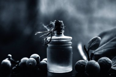 Şeffaf cam bir şişede banyan ağacı yağı ve biraz banyan meyvesi ile birlikte siyah parlak ahşap bir yüzey üzerinde yaprağını yakın çekim. Yatay çekim.