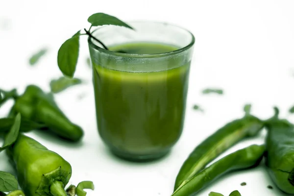 Hot, spicy, tangy and sweet green chili juice in a glass isolated. Horizontal shot of fresh-cut raw green chilis and its juice in a glass bowl on a white surface.Clipping mask.