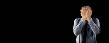 Embarrassed business employee worker wearing a corporate blue shirt with black necktie isolated on black background covering his face with his hands. Wide-angle shot. clipart