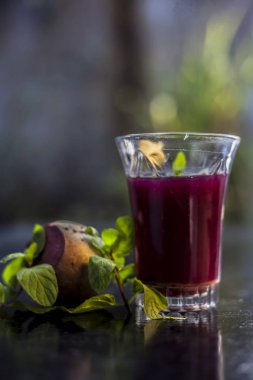 Sağlıklı pancar suyu, siyah parlak bir yüzey üzerindeki bir bardakta kilo vermek için biraz taze kesilmiş pancar kökü, biraz limon ve nane yaprağı. Arka planda bulanıklık olan dikey çekim..