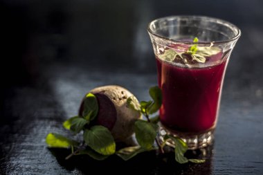 Healthy beetroot juice for weight loss in a glass on black glossy surface along with some raw fresh cut sliced beetroot vegetable some lemons, and mint leaves. clipart