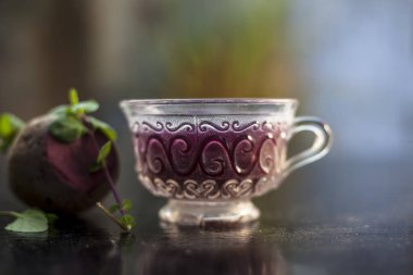 Best detoxify drink on a black glossy surface in a glass cup. Beetroot tea in a transparent glass cup on a black surface with a raw beet and some mint leaves. Horizontal shot with blurred background. clipart