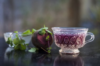 Best detoxify drink on a black glossy surface in a glass cup. Beetroot tea in a transparent glass cup on a black surface with a raw beet and some mint leaves. Horizontal shot with blurred background. clipart