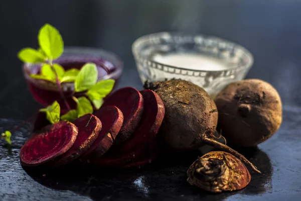 Beetroot face mask on the black glossy surface consisting of some grated beetroot vegetable and sour cream well mixed in a glass bowl along with raw cut sliced beetroot vegetable and cream.