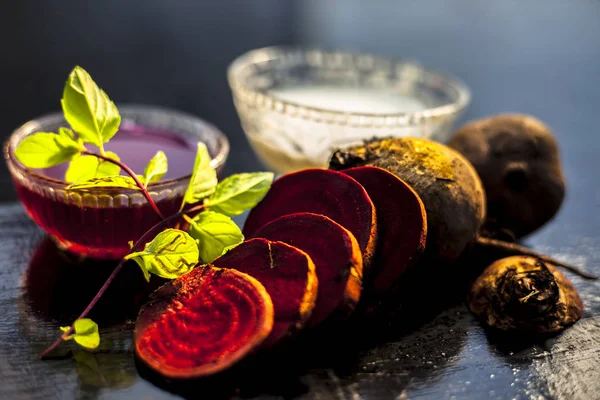 Beetroot face mask on the black glossy surface consisting of some grated beetroot vegetable and sour cream well mixed in a glass bowl along with raw cut sliced beetroot vegetable and cream.