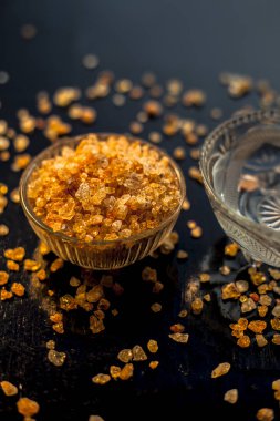 Gond katara / Gond Katira / Tragacanth Gum veya cam bir kasede yenebilir sakız ve sırt ağrısı için başka bir kasede biraz su. Siyah parlak bir yüzey üzerinde, yayılmış gond kristalleri ile..