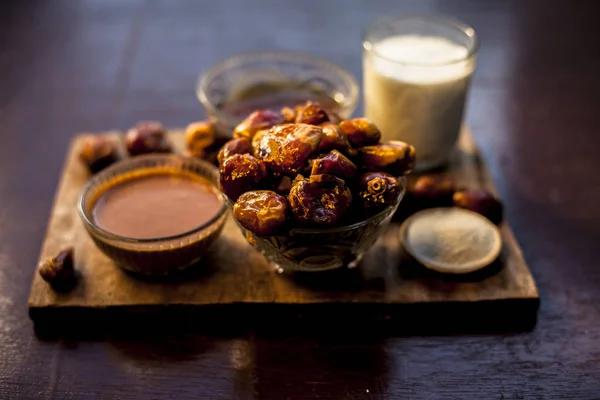 Dates face mask on a brown wooden surface with some golden light and selective focus consisting of some dates, milk, semolina, and honey. For softer and brighter skin. Horizontal shot.