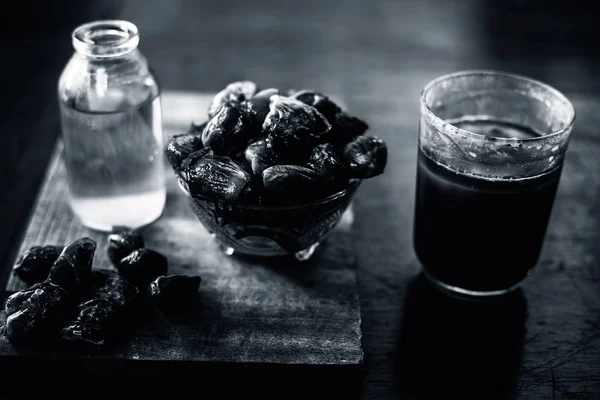 Dates syrup in a glass along with some raw dried dates and some cooking oil in a glass bottle on a wooden surface.Horizontal shot of date syrup with raw dried dates and cooking oil.