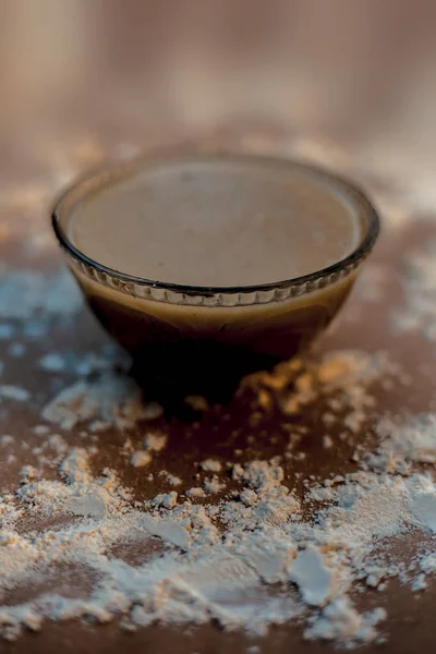 Close up of Indian desi winter drink Bajri Rabb winter drink or Bajri ki rabdi/rabri in a glass bowl along with some raw spread pearl millet flour and jaggery.On a  brown wooden surface.Vertical shot.