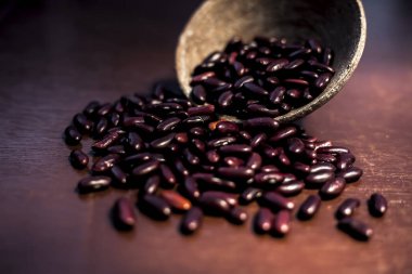 Kahverengi yüzeydeki çiğ böbrek fasulyelerini üzerinde spot ışığı olan kilden bir kaseyle kapat. Yatay çekim.