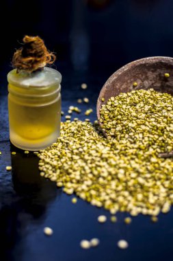 Yeşil gram, mung fasülyesi ya da moong fasulyesiyle dolu kil kasesini ve siyah bir yüzey üzerindeki cam bir şişede özütülmüş temel yağını kapatın. Dikey çekim.