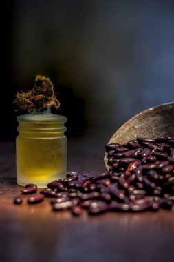 Kahverengi renkli yüzey üzerindeki çiğ fasulyeyi kilden bir kasede ve yağını üzerinde spot ışığı olan küçük şeffaf bir cam şişede kapat. Dikey çekim.