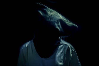 Adult human sitting on a rusted metal chair wearing a black colored bag covering his face.In dark gothic colors.