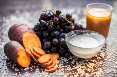 Anti-aging face mask with grapefruit on the black surface consisting of some carrot juice, sour cream, and rice flour. Shot of raw grapes and all other ingredients.