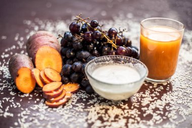 Anti-aging face mask with grapefruit on the black surface consisting of some carrot juice, sour cream, and rice flour. Shot of raw grapes and all other ingredients.