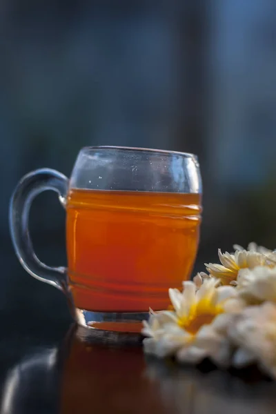 将菊花茶放在玻璃杯中 与一些常见的菊花一起放在黑色木板上的近照 背景模糊 焦点选择性强的垂直照 — 图库照片