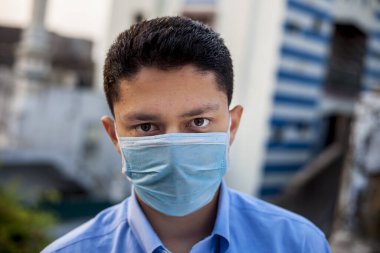 Mavi tişört giyen ve mavi maske takarak kendini koruyan sağlık düşkünü bir şirket çalışanının portresi. Covid 19 koruma ve Coronavirus hastalığını önleme.