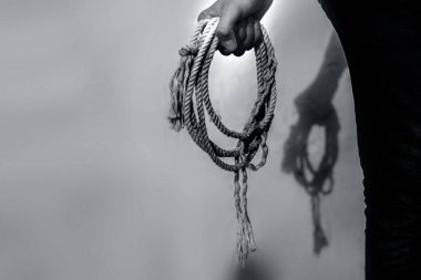 Erkek, elinde bir kement ya da kovboy halatı tutarken beyaz bir duvara karşı yakın çekim..